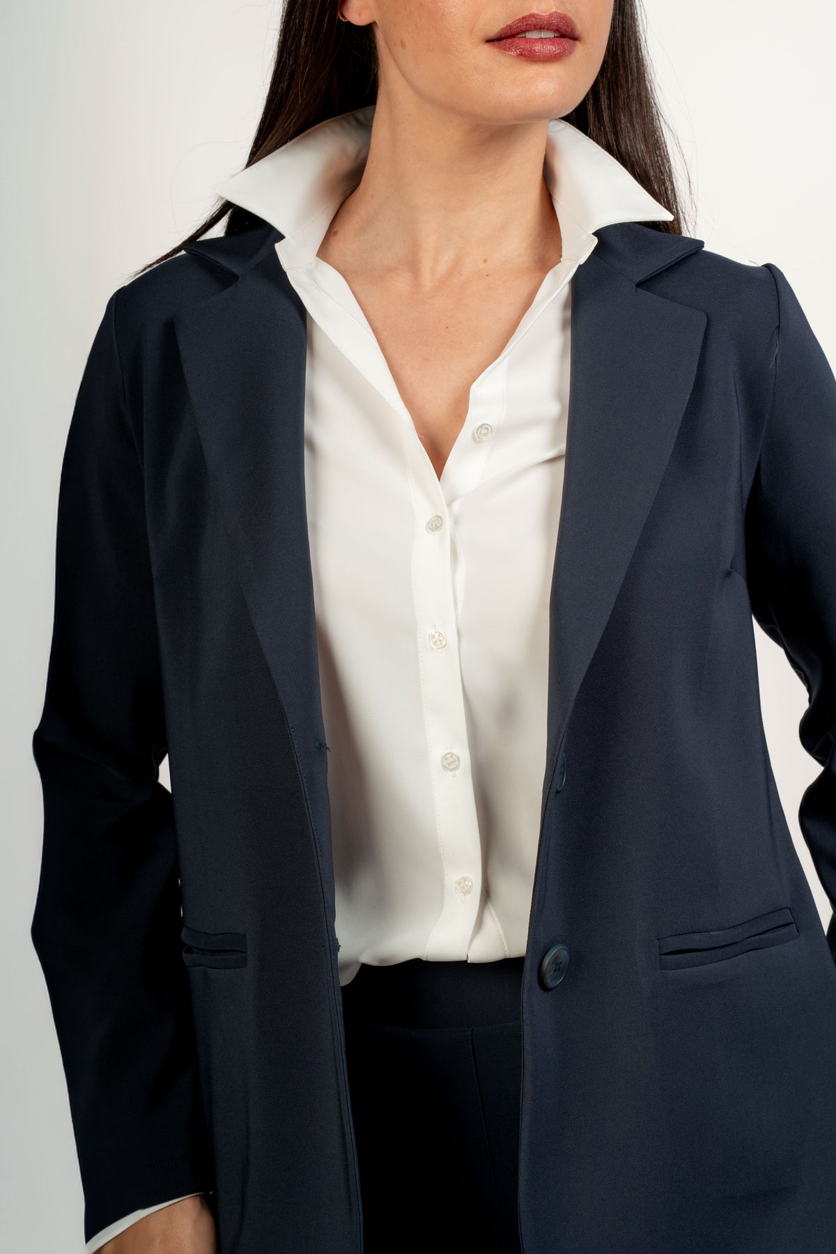 Camisa blanca abotonada bajo americana azul marino, detalle del cuello y la parte delantera