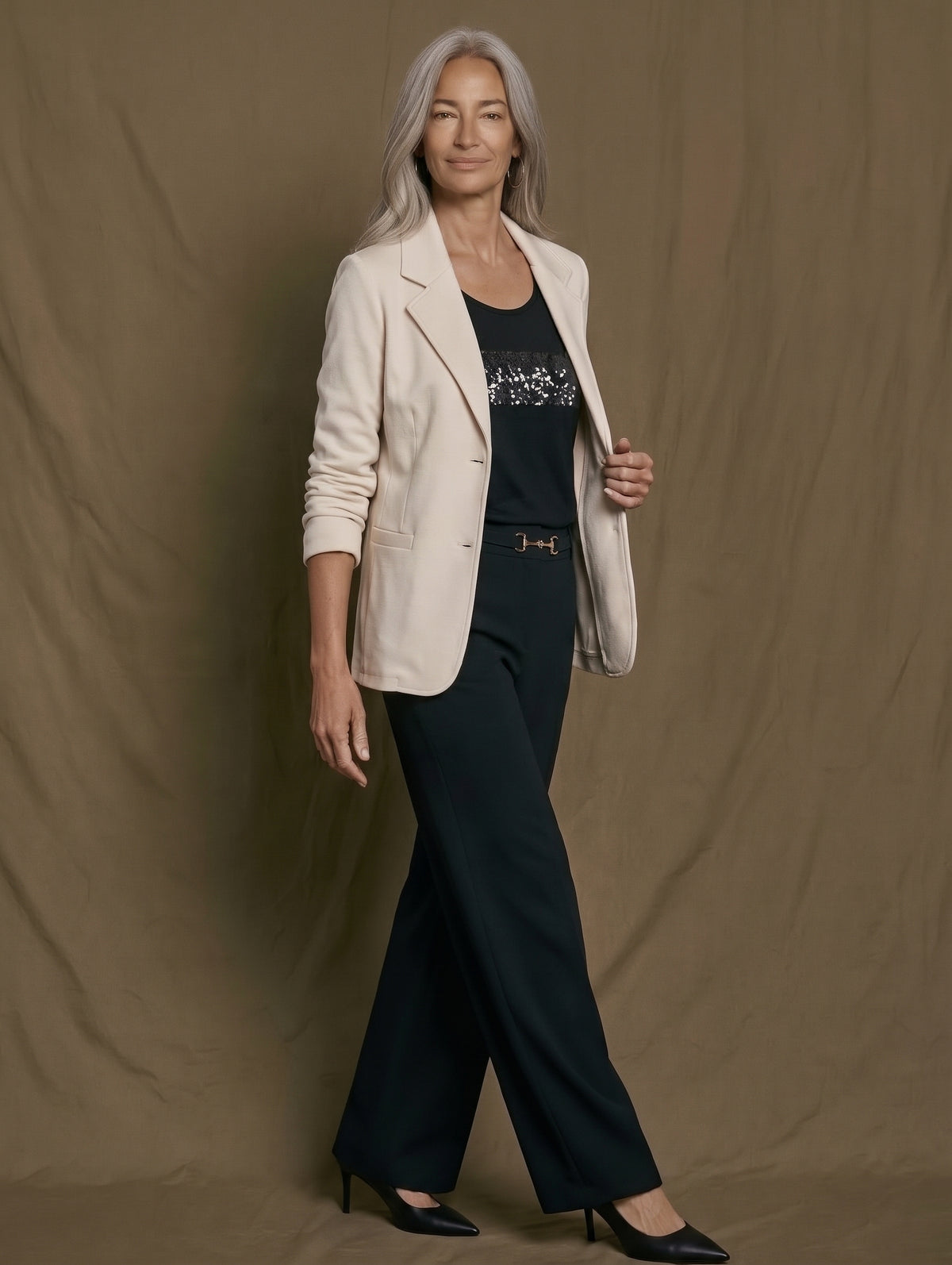 Pantalón ancho negro con americana crema, cinturón de hebilla dorada y salones, en movimiento
