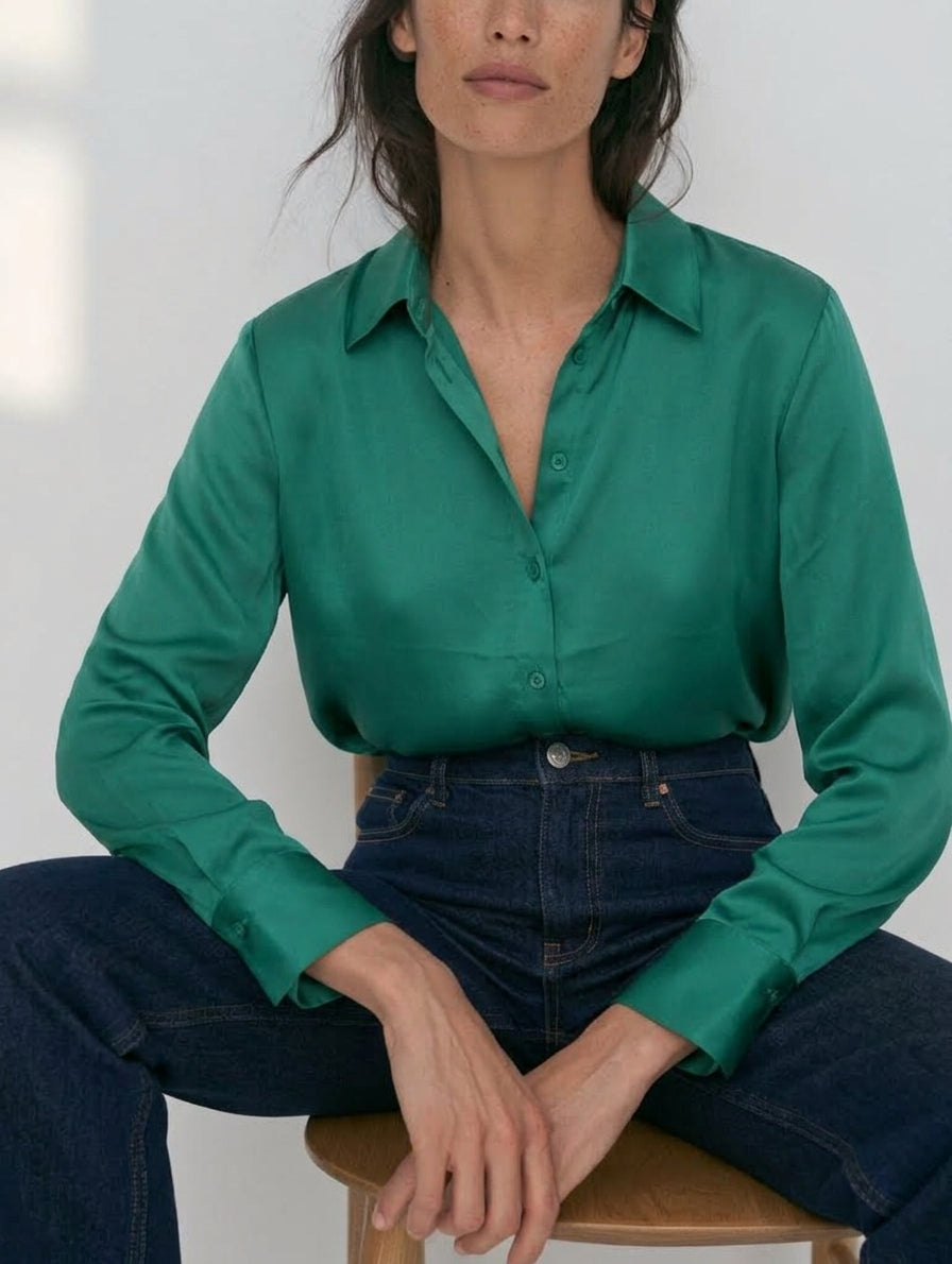Camisa satinada esmeralda para mujer con tejanos oscuros, plano medio sentada