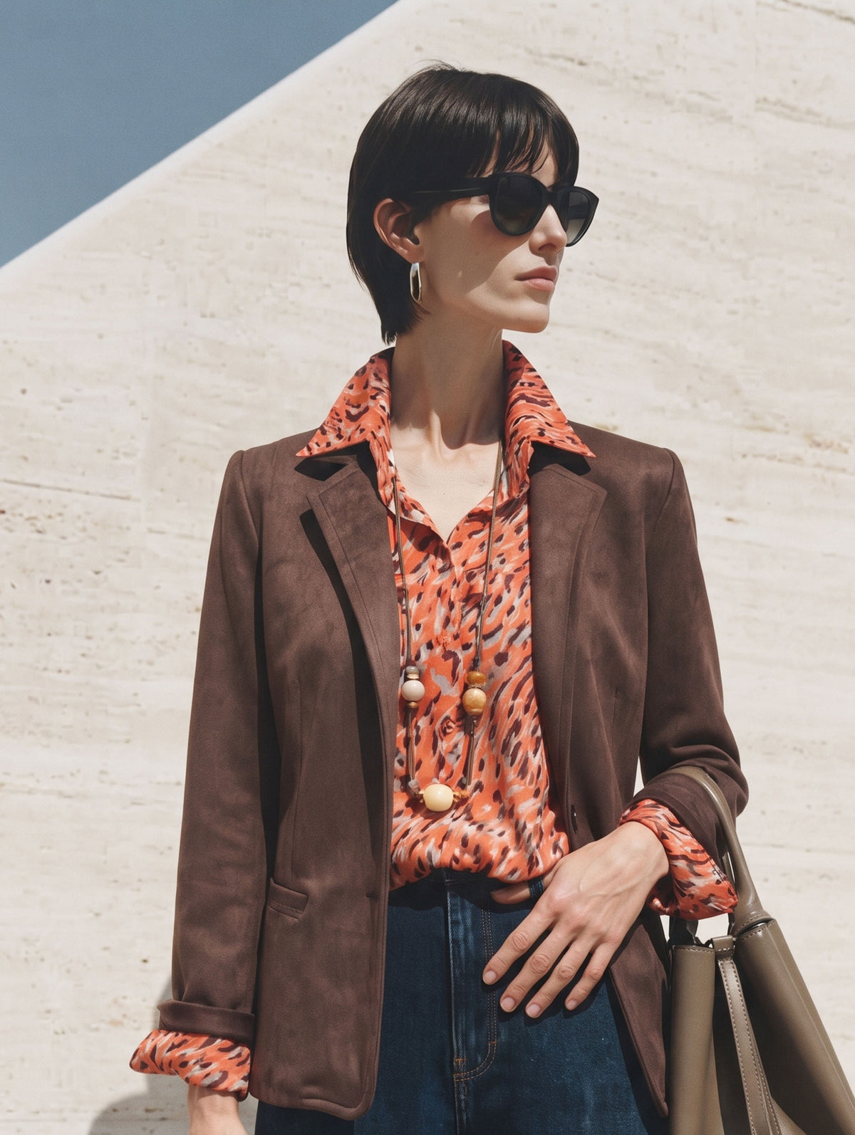 Americana de antelina marrón con camisa estampada naranja y gafas de sol, plano medio