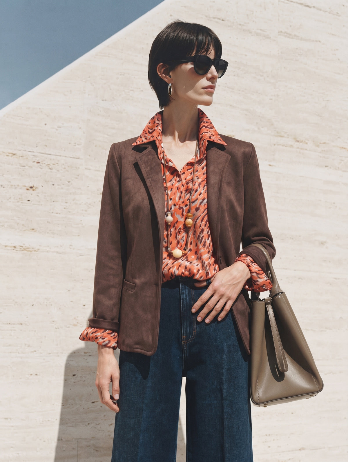 Americana de antelina marrón combinada con camisa estampada naranja, vaquero y bolso