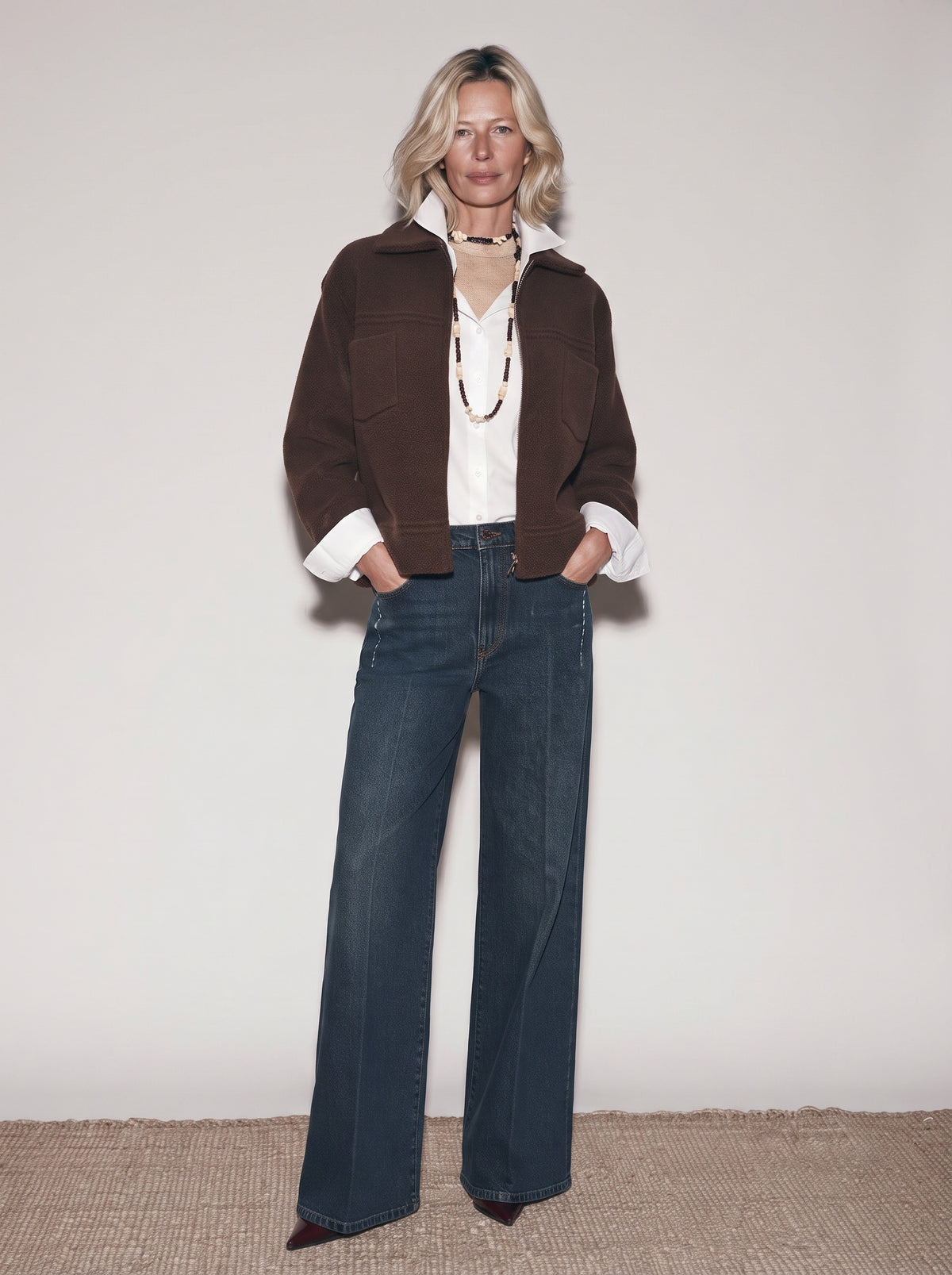 Chaqueta corta marrón para mujer con camisa blanca, collares largos y tejanos anchos, cuerpo entero