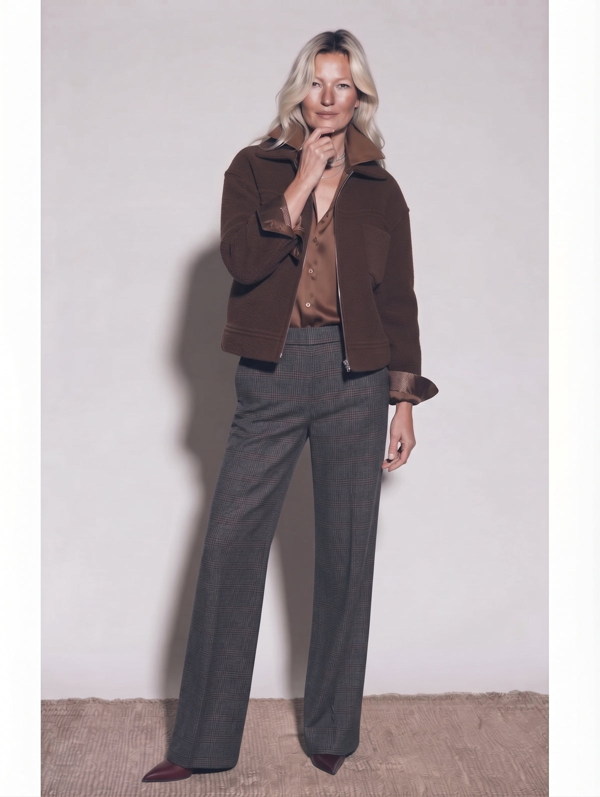Chaqueta marrón con cremallera sobre blusa satinada caramelo y pantalón gris de pernera ancha