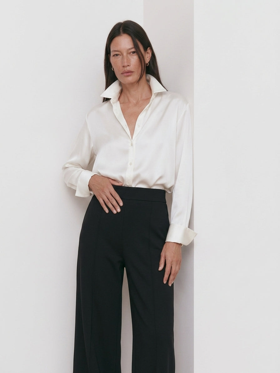 Camisa blanca para mujer con pantalón negro de pinzas, plano medio con la mano en la cintura