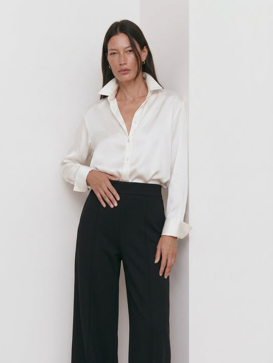 Camisa blanca para mujer con pantalón negro de pinzas, plano medio con la mano en la cintura