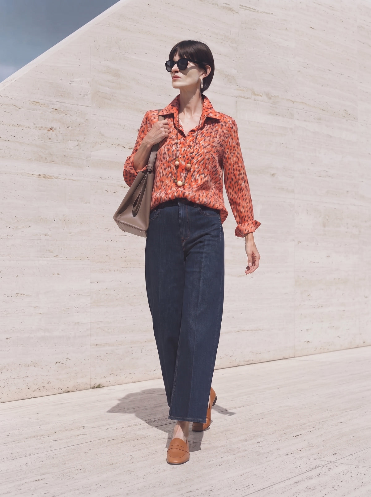 Camisa estampada naranja con tejanos anchos y mocasines marrones, caminando al sol