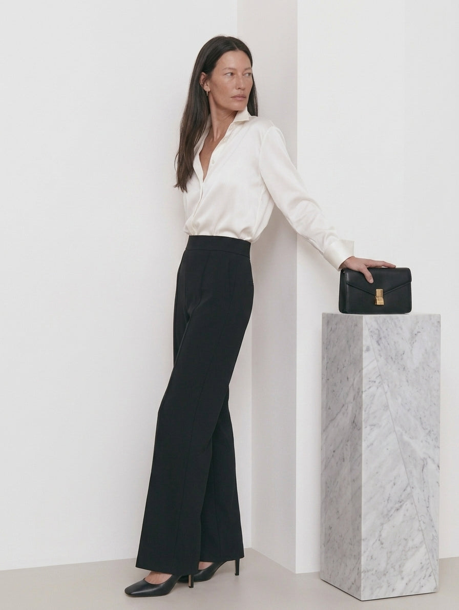 Pantalón recto negro de punto para mujer con camisa marfil y bolso negro, de perfil