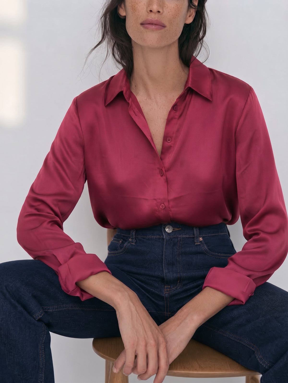 Camisa satinada frambuesa para mujer con puños vueltos y tejanos oscuros, plano medio sentada