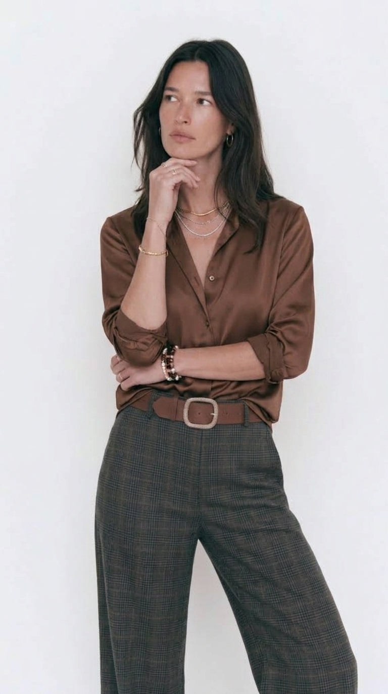 Pantalón de cuadros gris y marrón con camisa satinada marrón y cinturón, plano medio