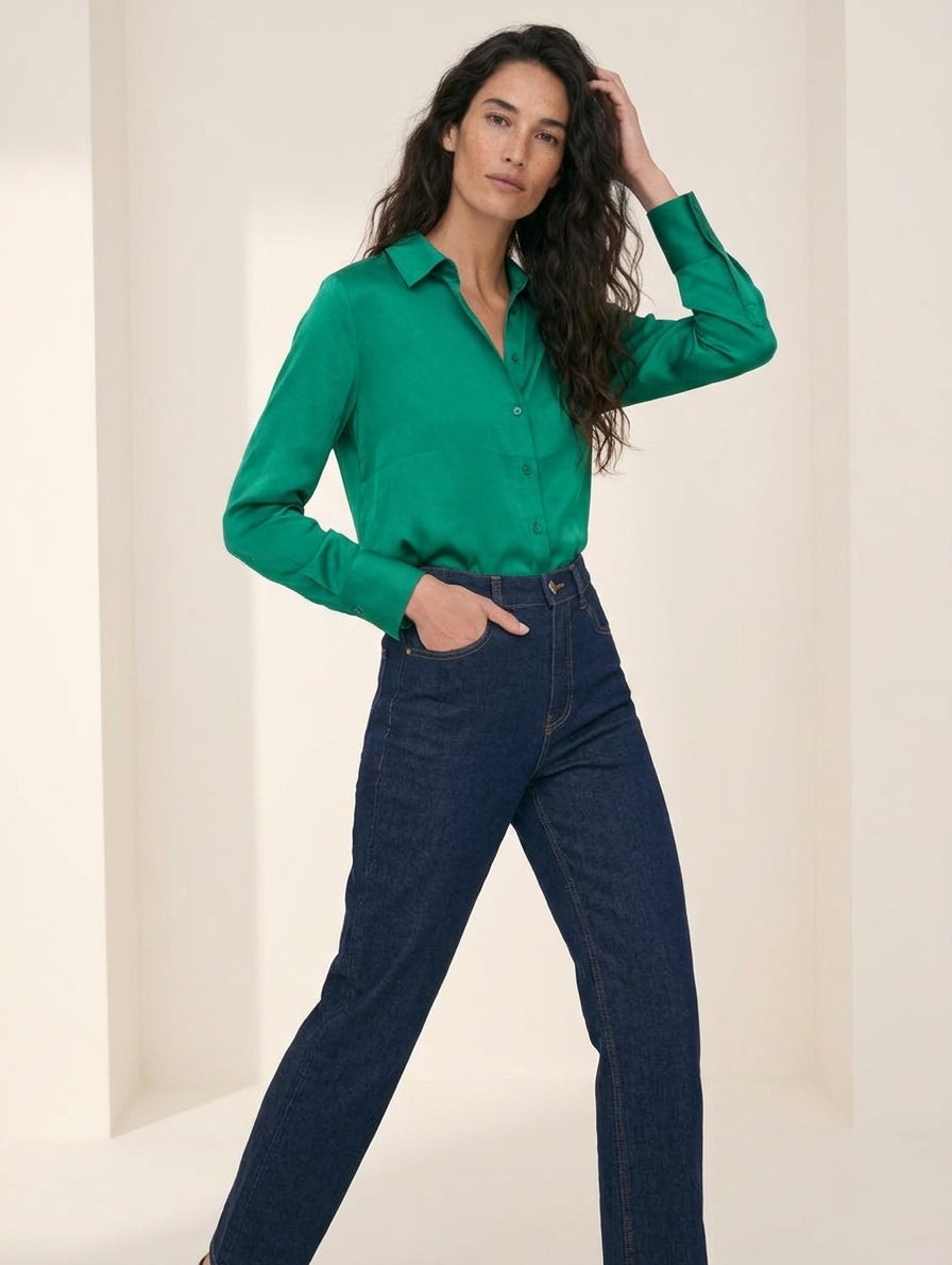 Camisa satinada esmeralda de manga larga con tejanos oscuros de tiro alto, de pie