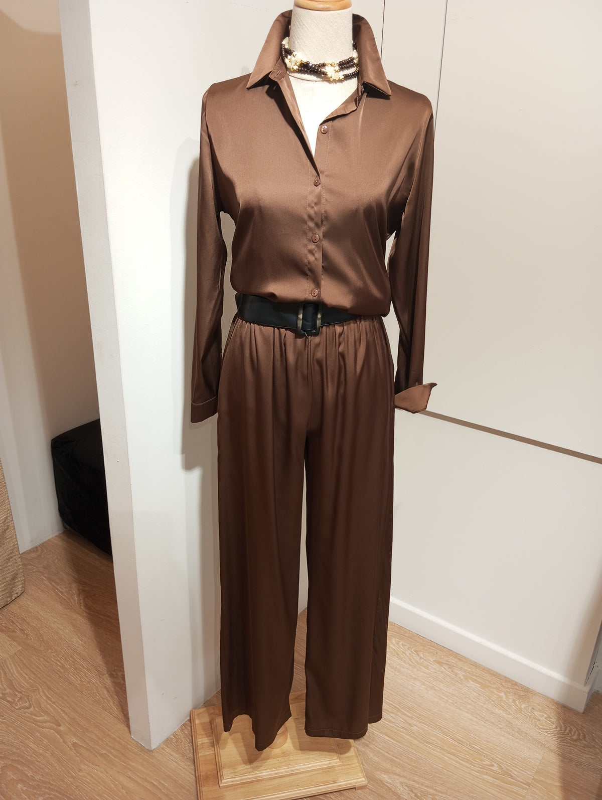 Camisa de raso marrón con pantalón a juego, cinturón negro y collar, en maniquí