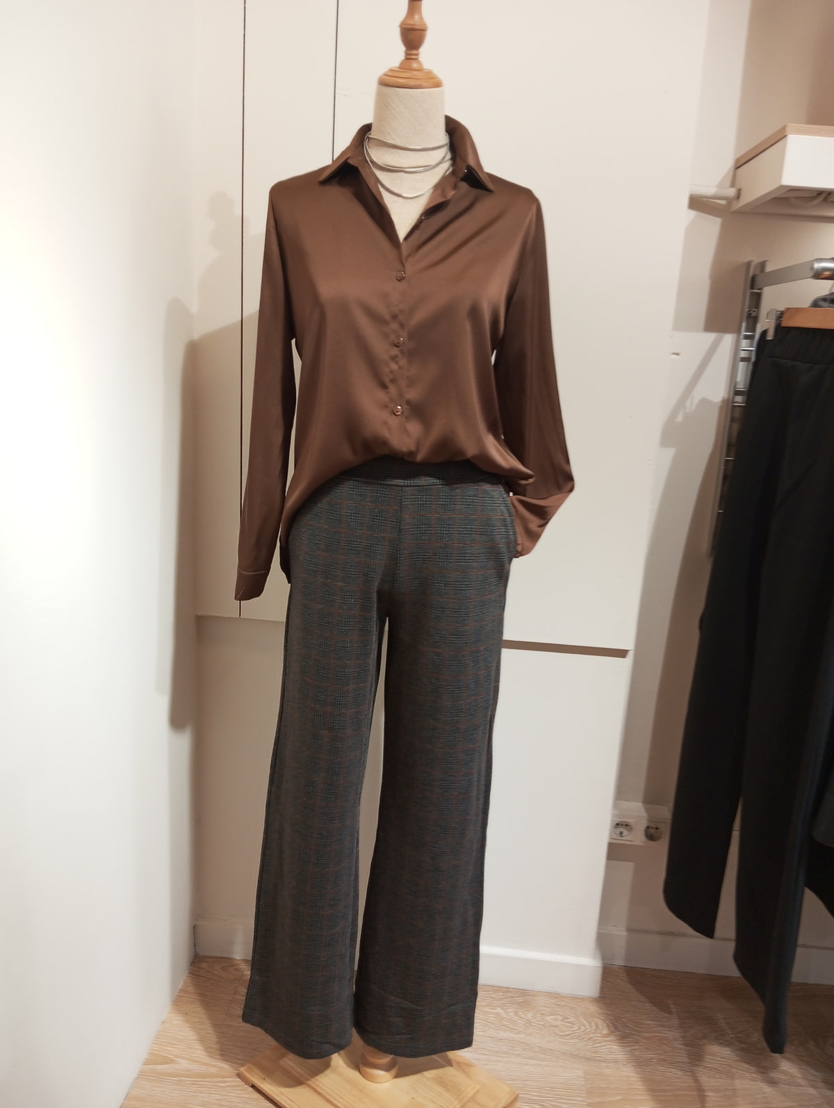Pantalón recto de cuadros gris con camisa satinada marrón por fuera, en maniquí