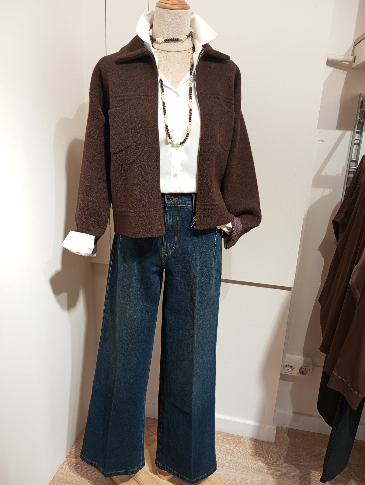 Chaqueta corta marrón con bolsillos de parche, camisa blanca y vaqueros anchos en maniquí