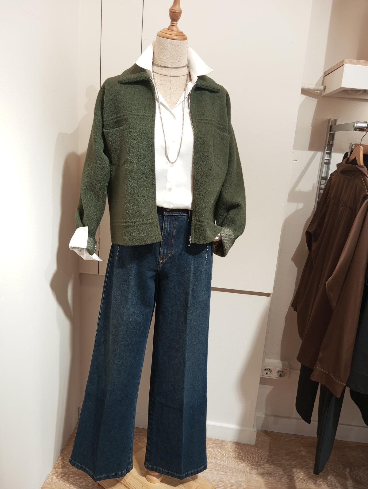Chaqueta corta verde kaki con bolsillos, camisa blanca y tejanos anchos en maniquí
