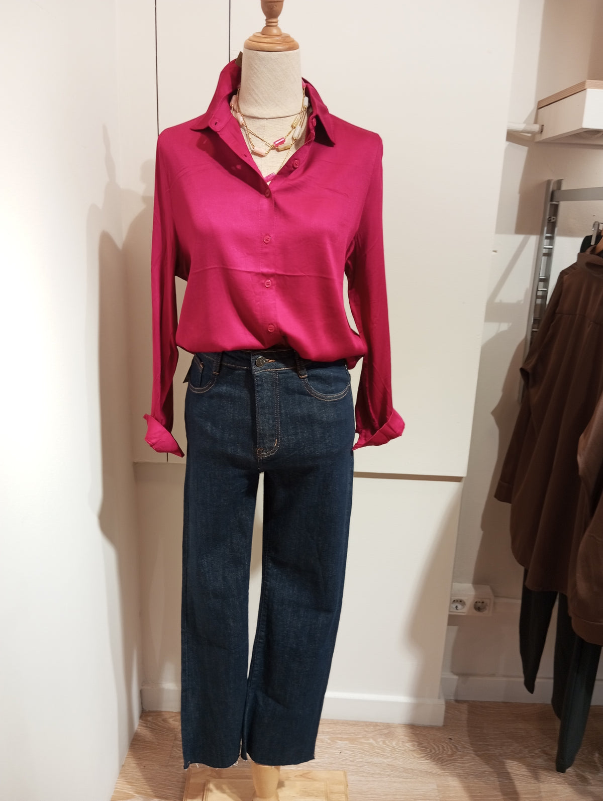 Camisa frambuesa de manga larga con collares y tejanos oscuros de bajo deshilachado en maniquí