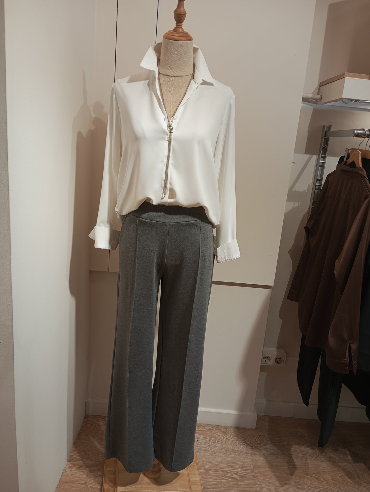 Pantalón de punto gris con costura central y blusa blanca con cremallera en maniquí