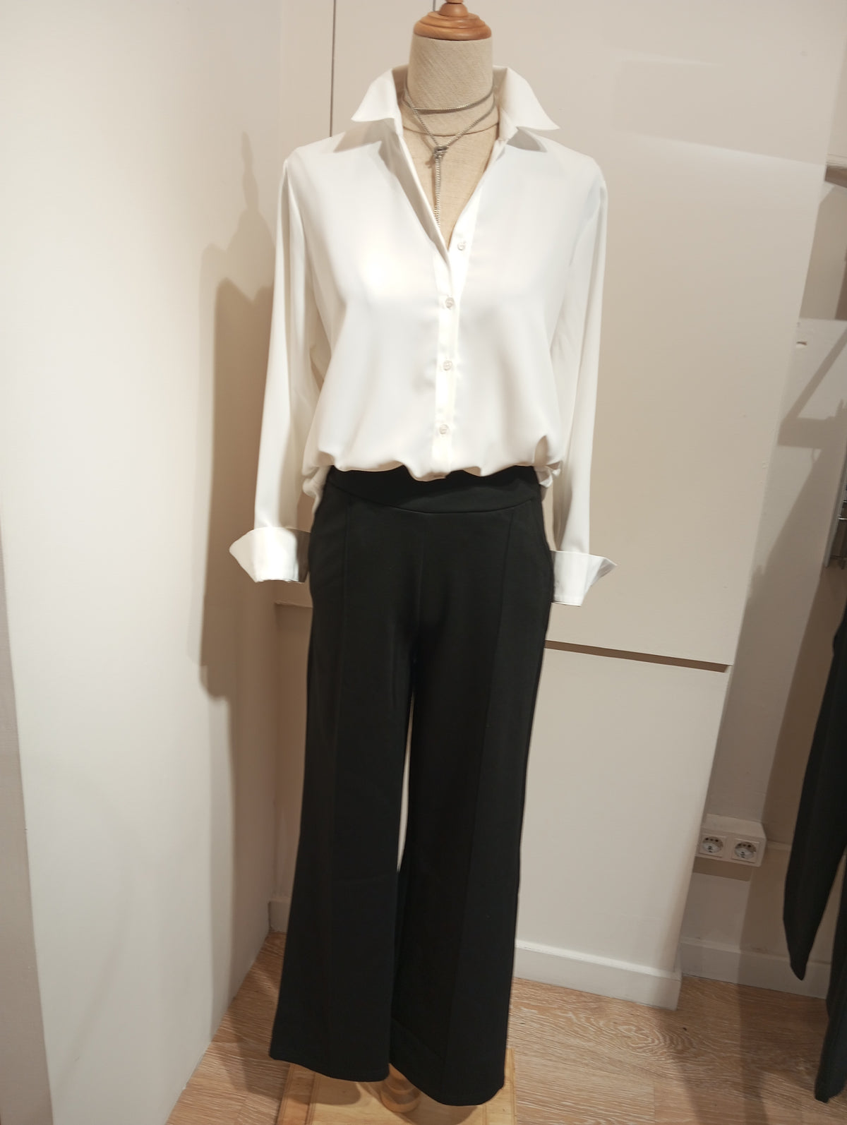 Pantalón negro de punto con costura frontal y camisa blanca de puños vueltos en maniquí