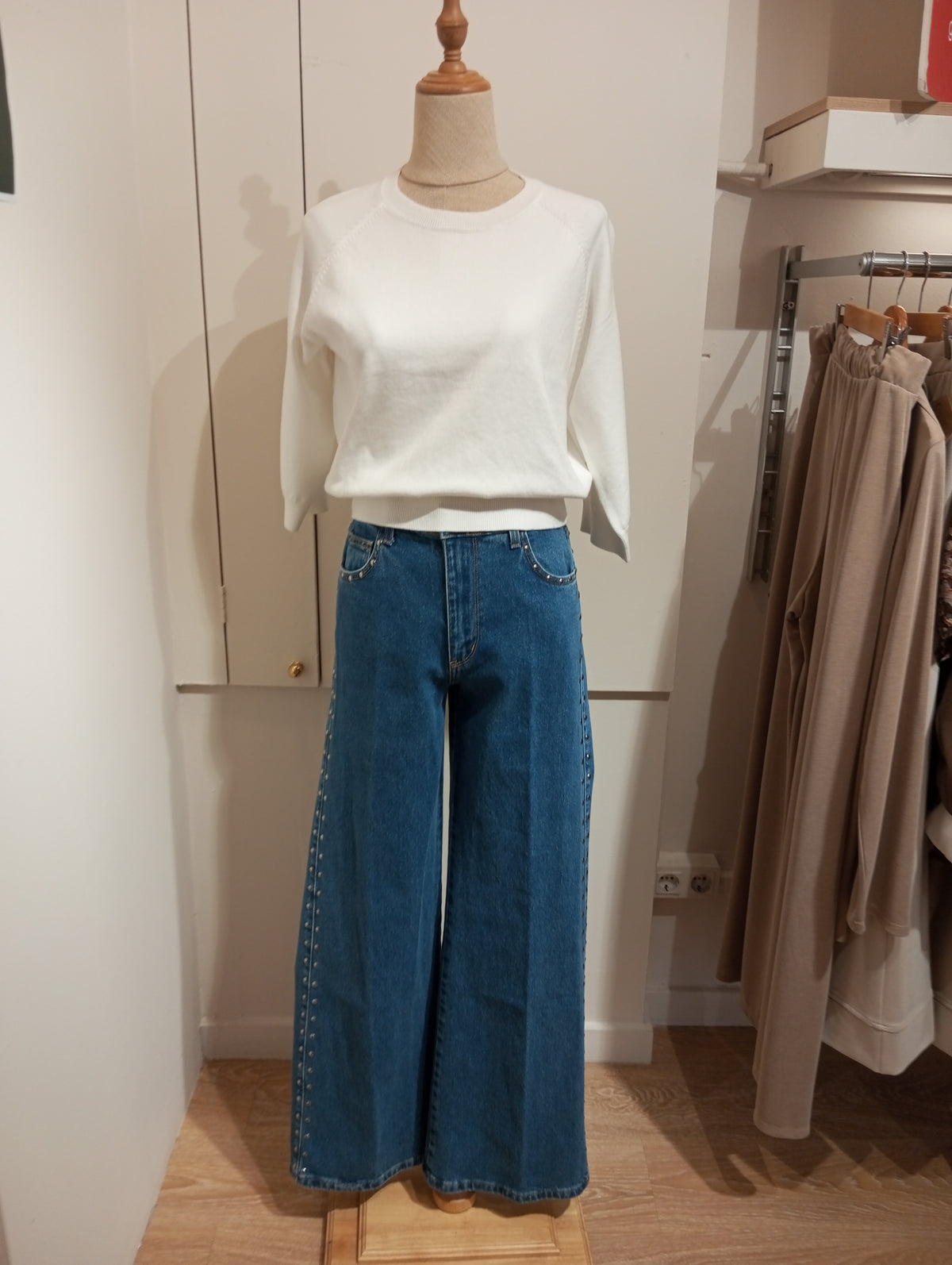 Jersey blanco de cuello redondo con vaqueros anchos de tachuelas laterales en maniquí