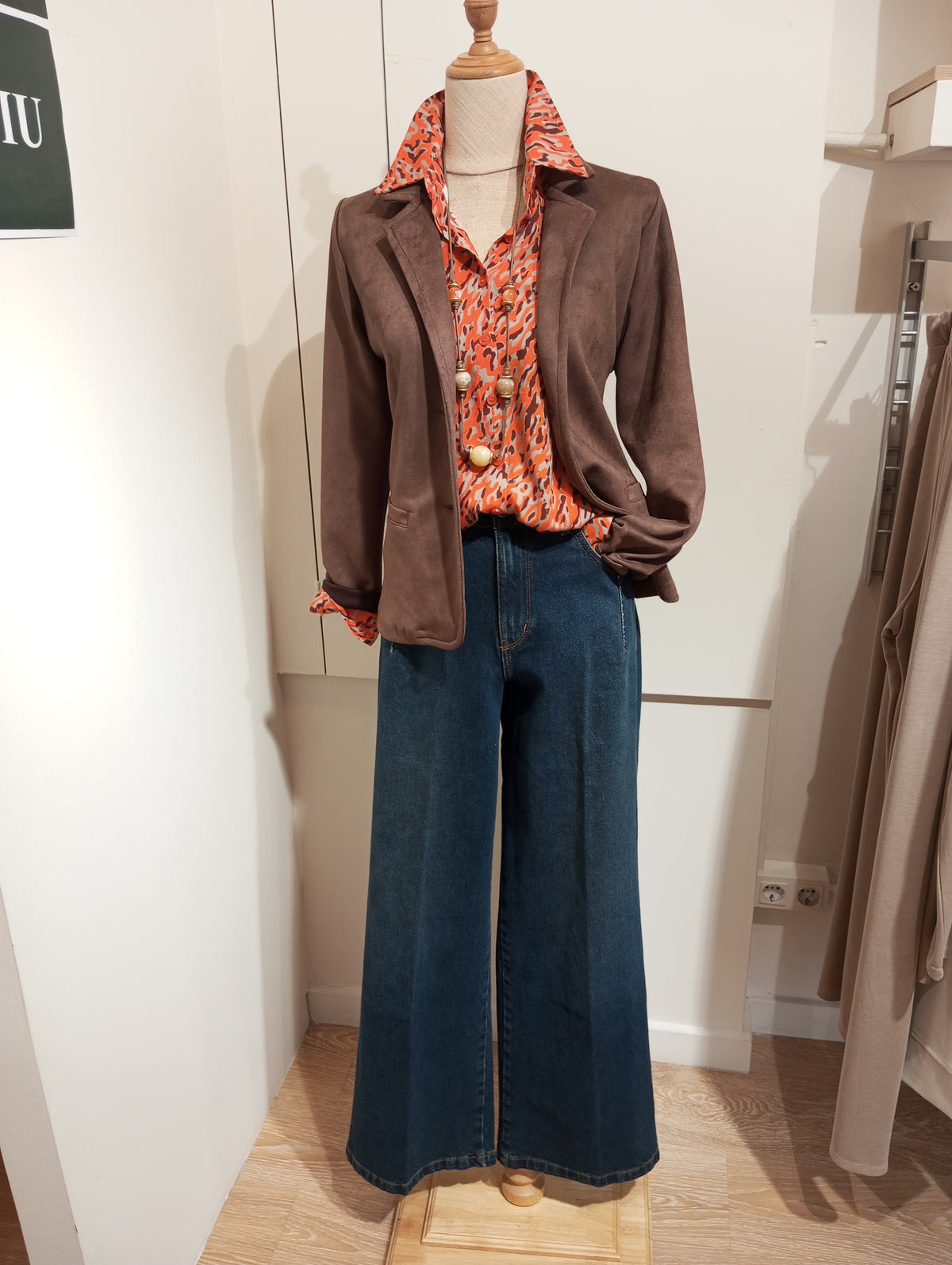 Americana de antelina marrón con camisa estampada y vaquero ancho en maniquí