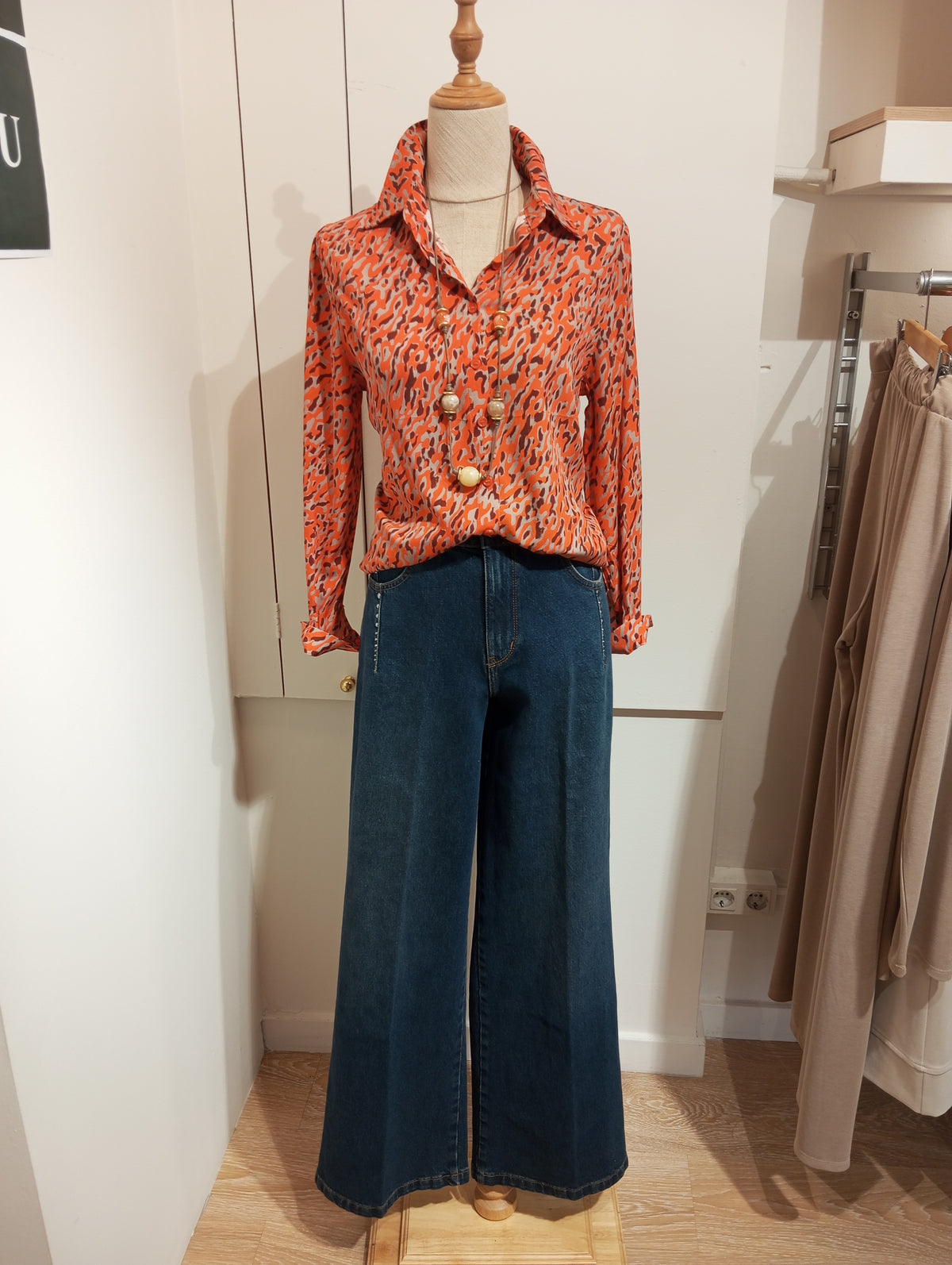 Camisa estampada naranja con collar de bolas y tejanos anchos en maniquí