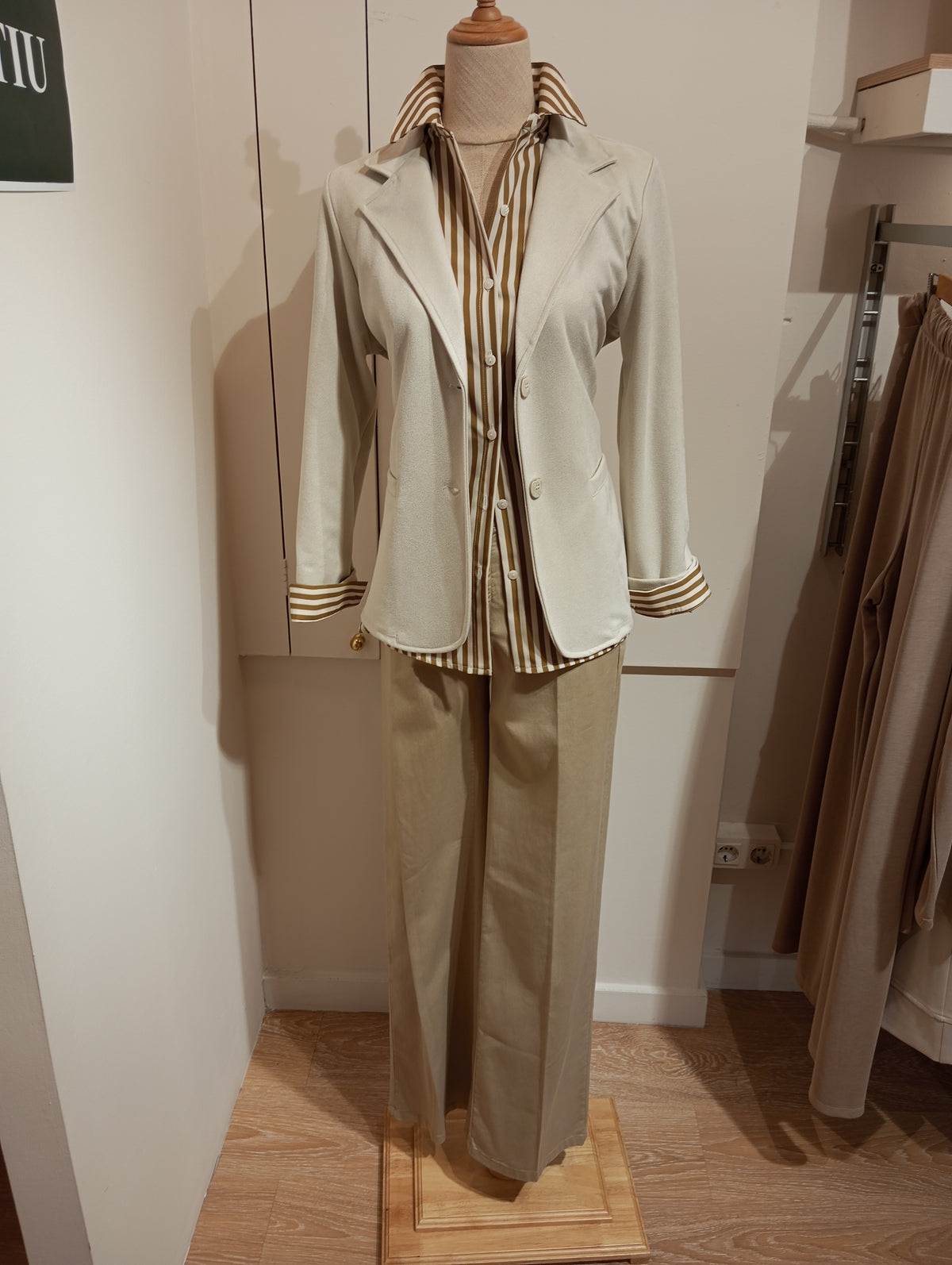 Pantalón recto beige con americana clara y camisa de rayas de cuello alto, en maniquí